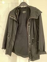 Front view of the black Mackage women's fall jacket hanging open on a hanger, showing zipper and snap-button closure with adjustable drawstrings at the waist.