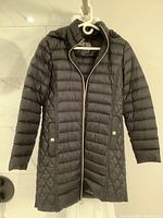 Front view of black Michael Kors women's jacket hanging, showing quilted design, zippered front with silver lining, and snap pockets.