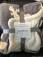 Folded WindRiver fleece sherpa blanket with grey and cream colors, moose pattern visible, secured with branded strap and label.