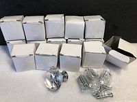 Photo showing 11 white boxes, 1 open box with a crystal knob and hardware laid out on a white cloth background.
