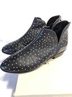 Side angled view showing black leather boots with silver studs on cream Kenneth Cole box.