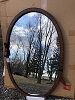 Full front view of the oval mirror reflecting outdoor scenery, showing the brown belt strap style metal frame.