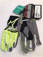 Pair of new Alpine Stars motocross gloves with tags showing the front and back side of the gloves in black and yellow colors.