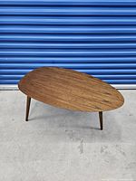 Front-angle view of wooden coffee table showing organic teardrop-shaped top and angled tapered legs.