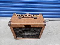 Front view of Kustom guitar amplifier showing brown textured vinyl covering and damaged grill cover with Kustom logo.