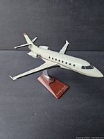 Front left angle view of the metal Marquis jet model and wooden stand on a black background.