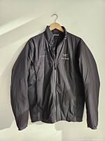 Front view of the black Arc'teryx insulated jacket hanging on a hanger showing the full jacket and front zipper.