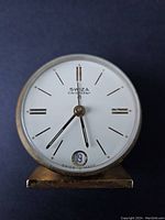 Close-up front view of Swiza calendar desk clock face showing hands, hour markers, and date window with number 19.