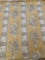 Close-up of fabric pattern showing rows of oval pastoral vignettes and floral motifs on mustard yellow background.