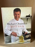 Front cover of Michael Chiarello's Bottega cookbook showing chef in white chef coat preparing food in kitchen.