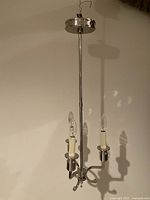 Full shot of polished nickel ceiling chandelier with three candle-style lights and upward-facing bulbs on a rod and circular canopy.