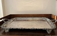 Angled front view of tray showing double handles, pierced border, scrolled feet and engraved surface.