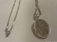 Close view of chain clasp and oval locket front showing engraved design