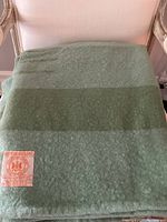 Folded green wool blanket with darker stripe and woven label visible