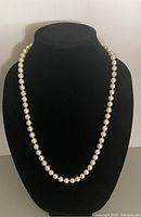 Full view of off-white pearl strand draped on black stand