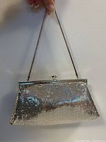 Front view of the silver mesh evening bag held by the chain handle against a wall showing the mesh and frame.
