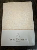 Top front view of folded sheet showing subtle Arabesque cream-yellow pattern and Yves Delorme branding on packaging.
