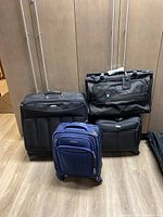 Photo showing five pieces of luggage including black and blue soft-sided rolling suitcases and duffel bag style luggage, tagged TUMI and Samsonite brands.