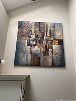 Front view of large abstract canvas painting mounted on a wall above a cabinet and next to a ceiling fan.