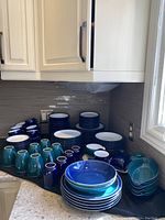 Front-left view showing rows of teal mugs, blue mugs and stacks of plates on countertop