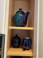 Photo showing the ceramic tea pot, creamer, and sugar bowl on shelves, all blue ceramic items with lid on pot and sugar bowl.
