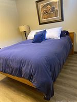 Three-quarter view of assembled wood bed frame with navy bedding in bedroom