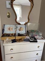 Wide view showing all jewelry boxes and containers on white dresser under gold-framed mirror. Items include beaded necklaces, bracelets, and multiple jewelry storage boxes.