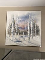Front view of the large square birch tree print mounted on a beige wall above a laundry machine, showing snowy landscape with bare birch trees and distant mountains under a dusk sky.