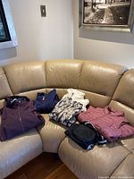 All six items arranged on couch: two puffer jackets, shell, patterned jacket, sweatshirt and pouch