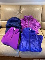 Four Lululemon outerwear items displayed on sofa: three jackets and one vest in purple, blue, and magenta tones.