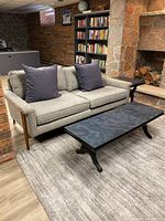 Front left-angled view of sofa showing grey upholstery, wood legs, and two blue pillows