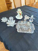 Wide shot showing three crystal lotus candle holders at left, ceramic angel at back, Swarovski lion and angel figurines at right and divided glass tray with small angels at front.