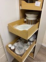 Two wooden drawers in cabinet showing bowls, casserole dish, platter, mugs and shakers partially wrapped