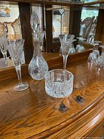Waterford crystal decanter with stopper, champagne flute, white wine glasses, round candy dish, and decorative bowl displayed on wood surface with mirrored background.