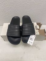 Top down view of the Adidas black slide sandals with box and size tag visible.