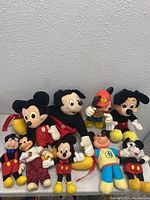 Front view of all nine Mickey Mouse plush toys arranged on a table showing size and outfit variations