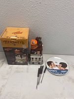Photo showing the Hershey's fondue set with original box and four black-handled fondue forks arranged beside it on a white surface against a grey wall.