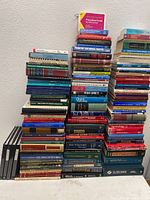 Three large stacks of medical textbooks and reference books on a carpeted floor against a white wall, titles visible include surgery, pathology, and vascular disease topics.