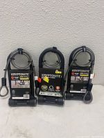 Three Kryptonite U-lock bike locks new in packaging with coiled double-looped cables wrapped around each shackle.