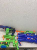 Wide view of 6 toy blasters in blue, green, and orange on white surface