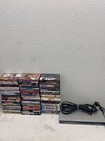 Stack of 82 DVDs with visible spines showing various titles, next to DVD player