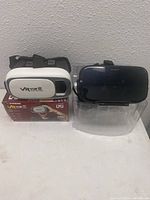 Two VR viewers side by side on a white surface; one white XTREME VR Vue II viewer with original box, and one black generic VR headset.