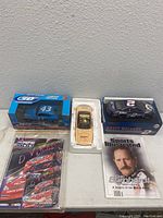 View showing three NASCAR die cast cars including a Richard Petty Plymouth Superbird, a Rusty Wallace car, and a gold-colored car, along with two DVDs and a magazine.