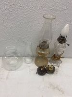 Oil lamps, glass chimneys and metal burner parts arranged on table showing all components in lot.