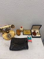 Shows entire lot including vintage rotary phone, Singer oil can, Majesta pocket watch with case, Camel cigarette tin, small bottle, wooden brush, and black leather pouch.