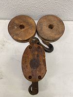 Top view of two wooden wheels and wooden pulley block with attached metal hook on a white surface against textured wall.