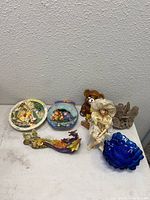 Photo of collectible plates, porcelain doll, teddy bear figurine, dragon figurine, glass bowl and tree stump sculpture