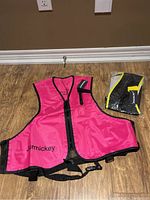 Pink snorkel swim vest laid flat on the floor next to black and yellow vest still packaged.