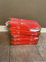 Stack of five packs of Staples copy paper on tile floor, packaging torn on several packs