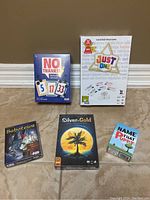 Five boxed board and card games arranged on floor against wall, original packaging, colorful box art.